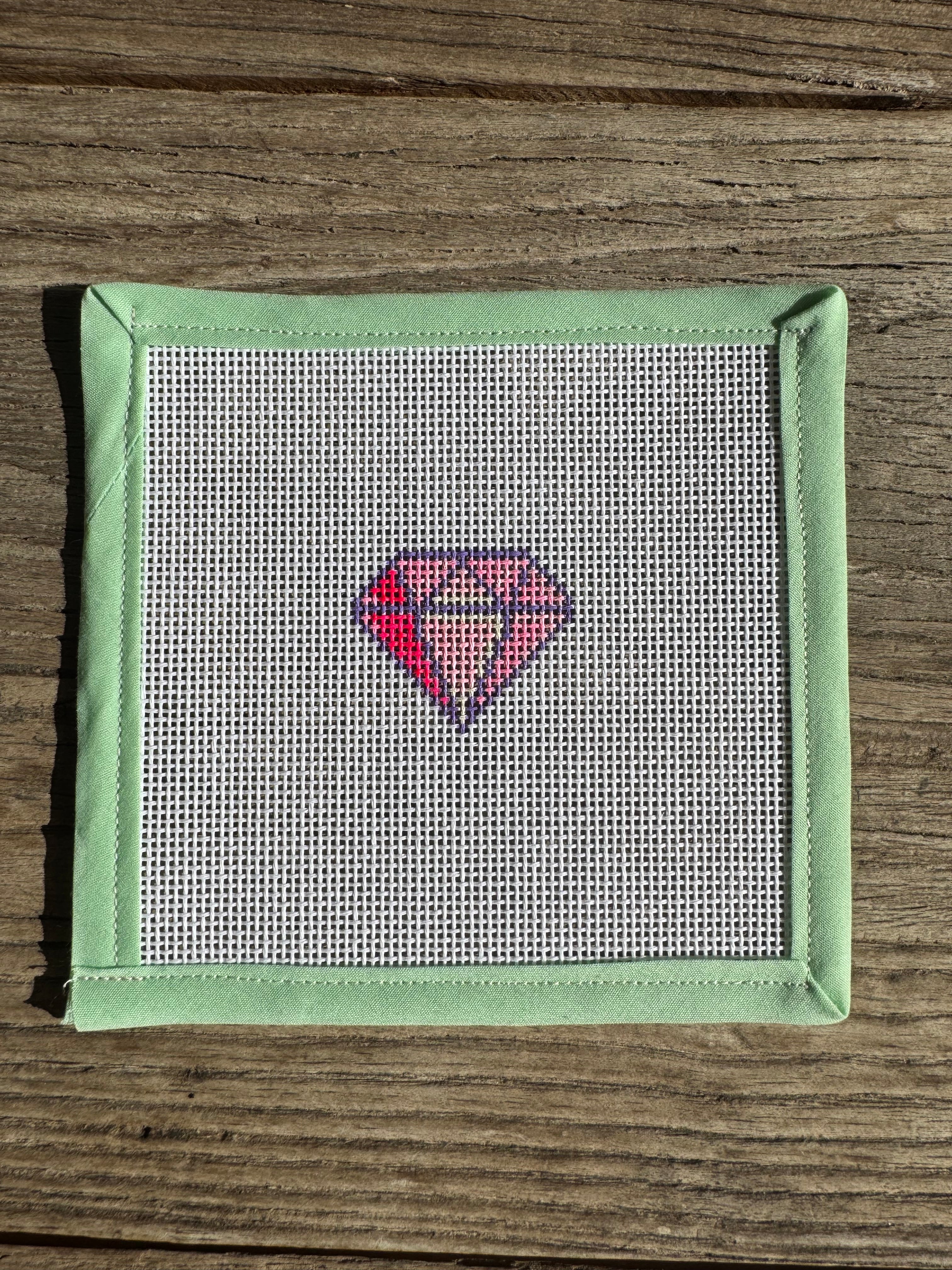 needlepoint  diamond pattern on fabric with green frame on wooden surface