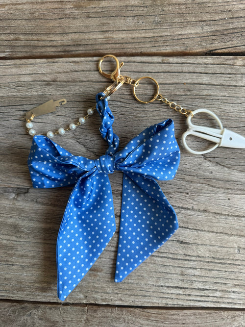 Blue polka dot bow keychain on a wooden surface with scissors in the background