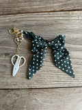 Black polka dot scrunchie with white scissors charm on a wooden surface