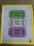 A square white needlepoint canvas with a yellow border, featuring three colorful ticket designs stacked vertically. The top green ticket reads 'HAUNTED HOUSE', the middle white ticket with red border reads 'GHOST TOUR', and the bottom purple ticket with orange border reads 'SERANCE NIGHT'.