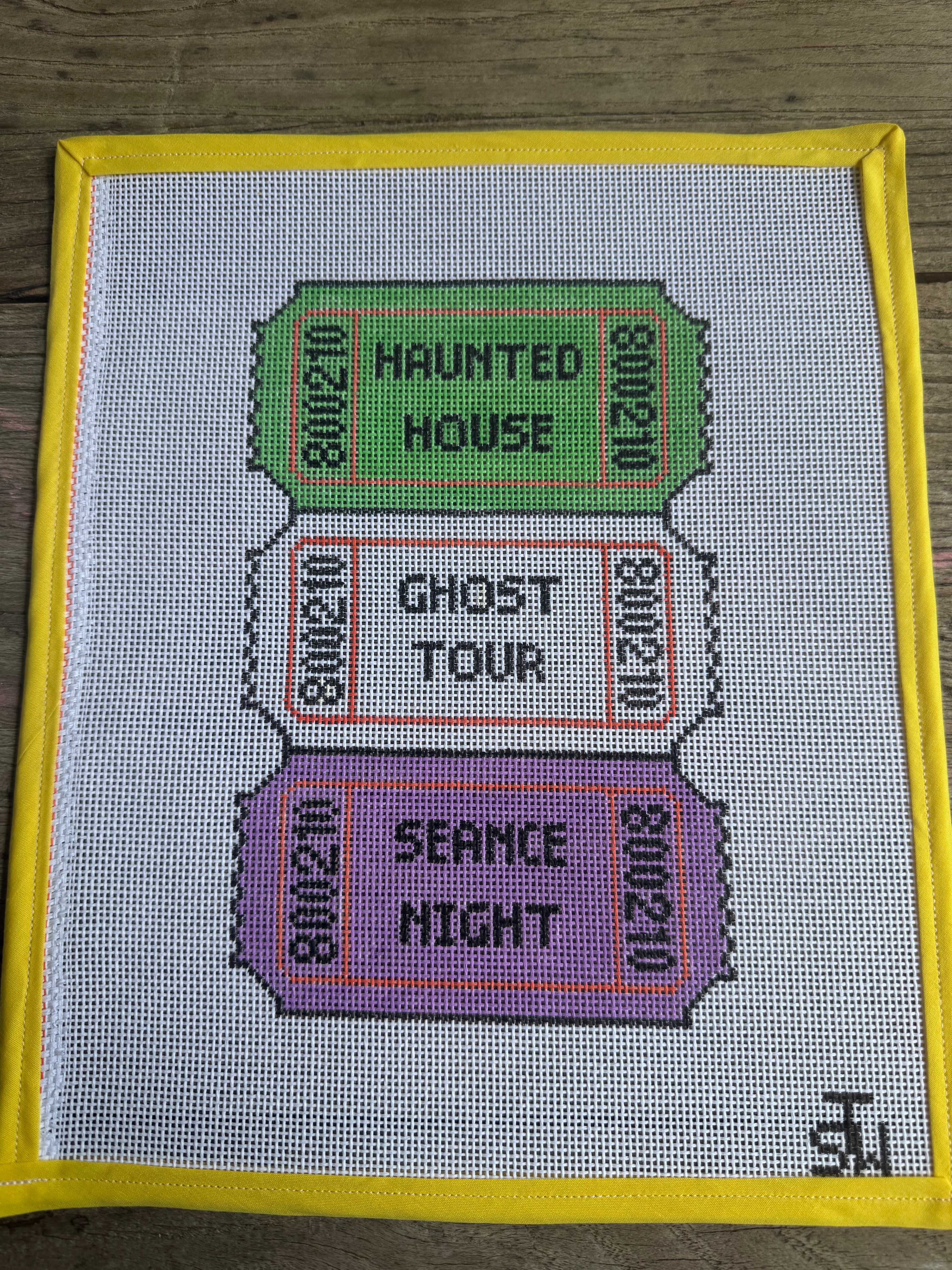 A square white needlepoint canvas with a yellow border, featuring three colorful ticket designs stacked vertically. The top green ticket reads 'HAUNTED HOUSE', the middle white ticket with red border reads 'GHOST TOUR', and the bottom purple ticket with orange border reads 'SERANCE NIGHT'.