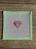 needlepoint  diamond pattern on fabric with green frame on wooden surface