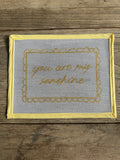 Decorative mesh panel with embroidered text on a wooden surface
